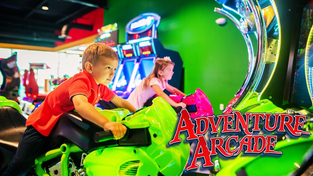 Children riding green arcade racing machines with 'ADVENTURE ARCH' text. 2