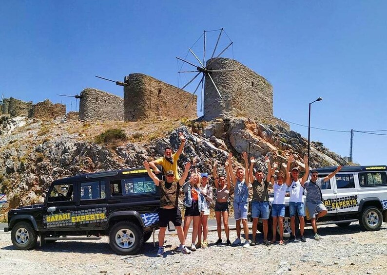 A group of people posing in front of a windmill and a safari vehicle. 1