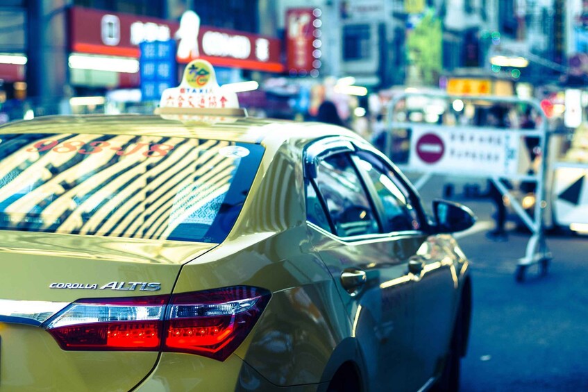 A yellow taxi with a sign on top, a rear view of a vehicle, and a 'no entry' sign in the background. 2