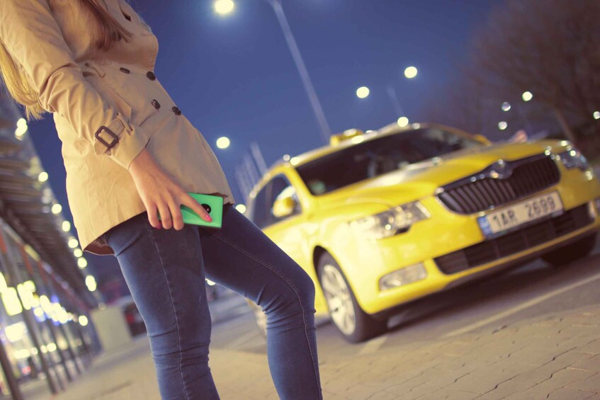 A person holding a green smartphone, standing on a sidewalk with a yellow taxi in the background. 5