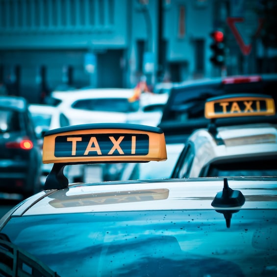 A taxi with a 'TAXI' sign on its roof, surrounded by other vehicles on a city street. 1