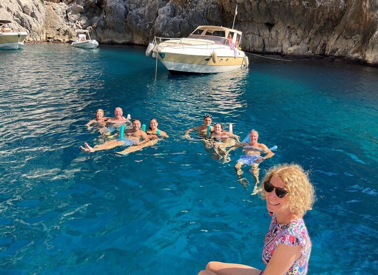 A group of people floating on a boat in clear blue water with rocky cliffs in the background. 5