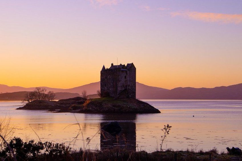 A castle on an island with a calm lake and mountains in the background. 2