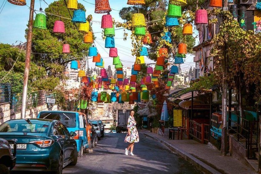 A street with colorful hanging lanterns, parked cars, and a pedestrian. 2
