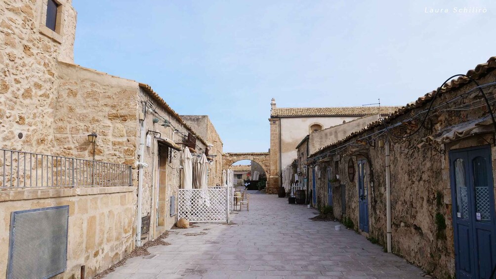 Una stretta via in pietra fiancheggiata da edifici, un cancello e un arco in lontananza. 3