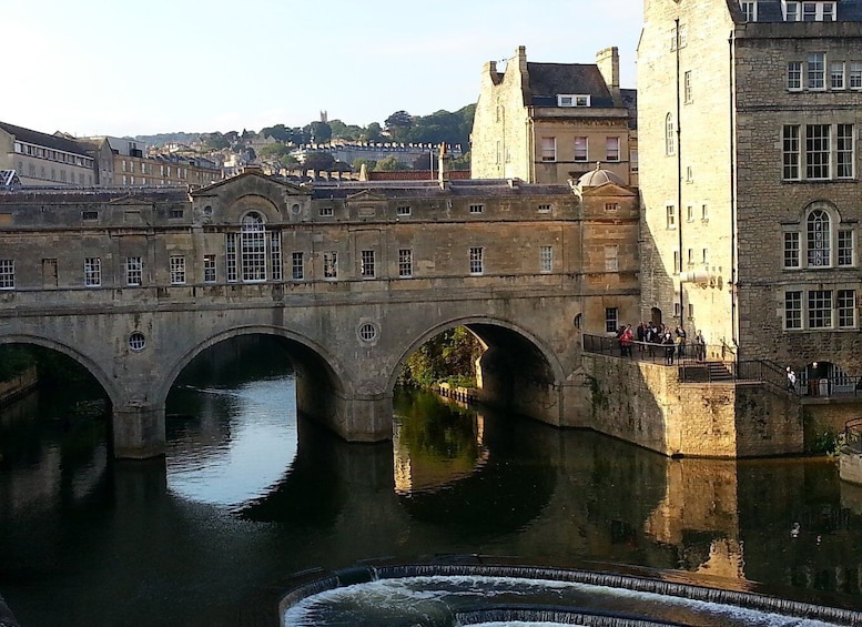 A stone bridge over a river with arches, a castle-like building, and a group of people on a balcony. 5