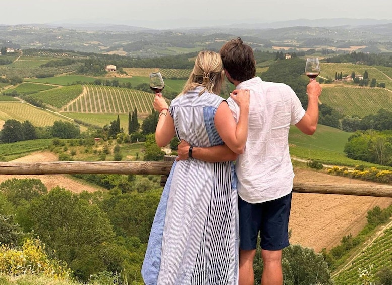 A couple standing on a wooden fence overlooking a vineyard with rows of grapevines. 1