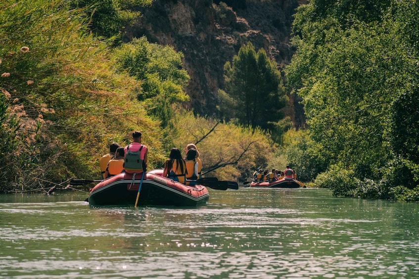 People on inflatable boats in a river surrounded by dense greenery and cliffs. 2