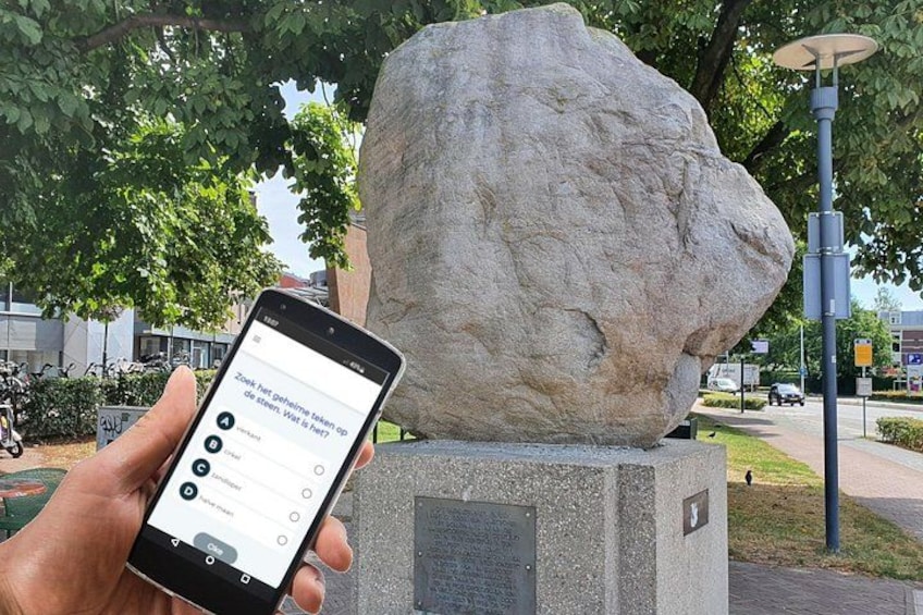 A hand holding a smartphone with a question about a stone monument. 1