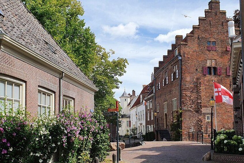 A cobblestone street lined with historic brick buildings, a flag, and blooming flowers. 4