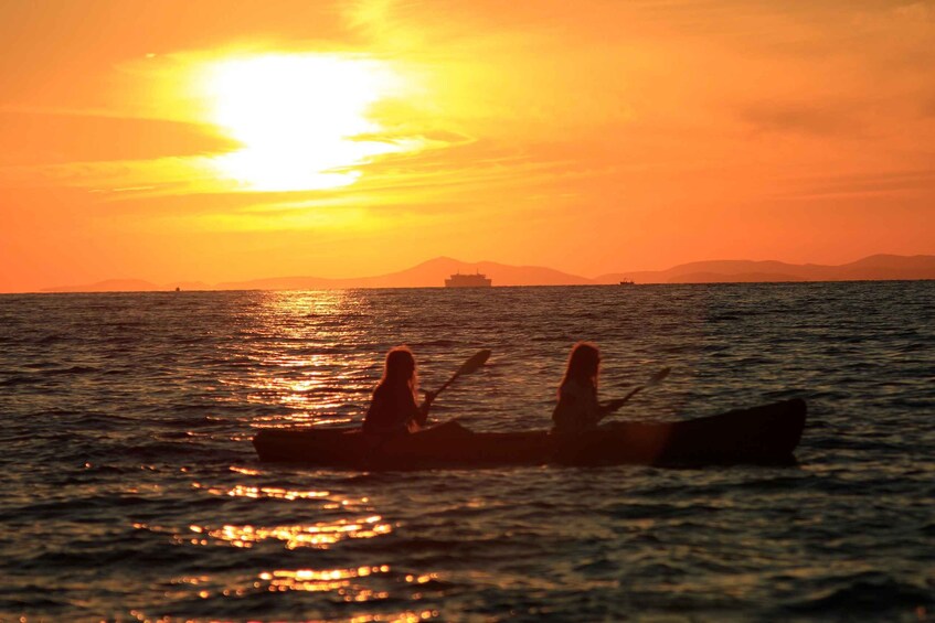 A sunset over the ocean with a boat and two people in the foreground. 2