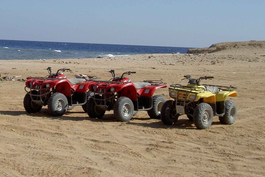 Cuatro cuatrimotos estacionadas en una playa arenosa con el océano al fondo. 2