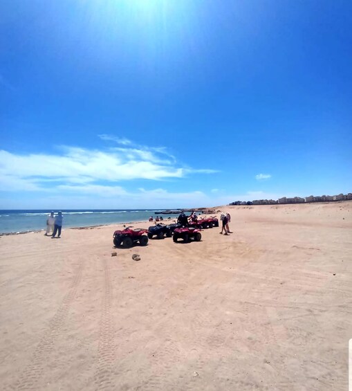 Una playa arenosa con cielo despejado, algunas personas y varios cuatrimotos estacionadas. 3