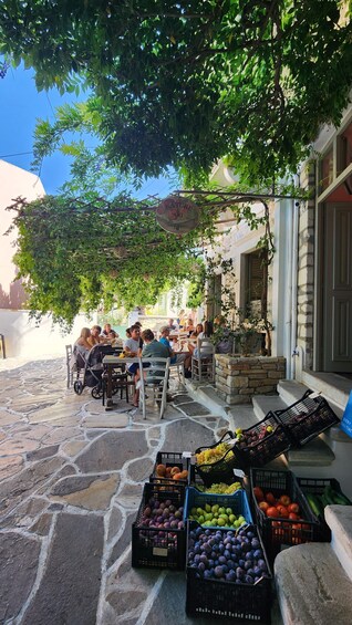 Outdoor seating under a tree, surrounded by stone pavement, with crates of fruits and vegetables. 2