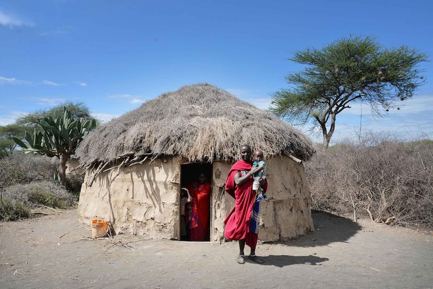 A person in traditional attire standing in front of a thatched hut with a child. 3