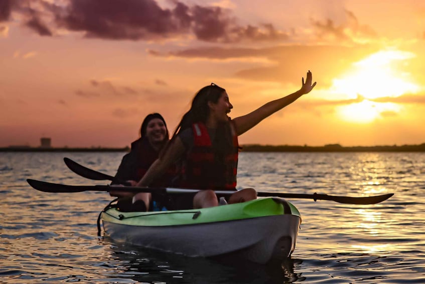 Two people kayaking on a body of water during sunset. 1