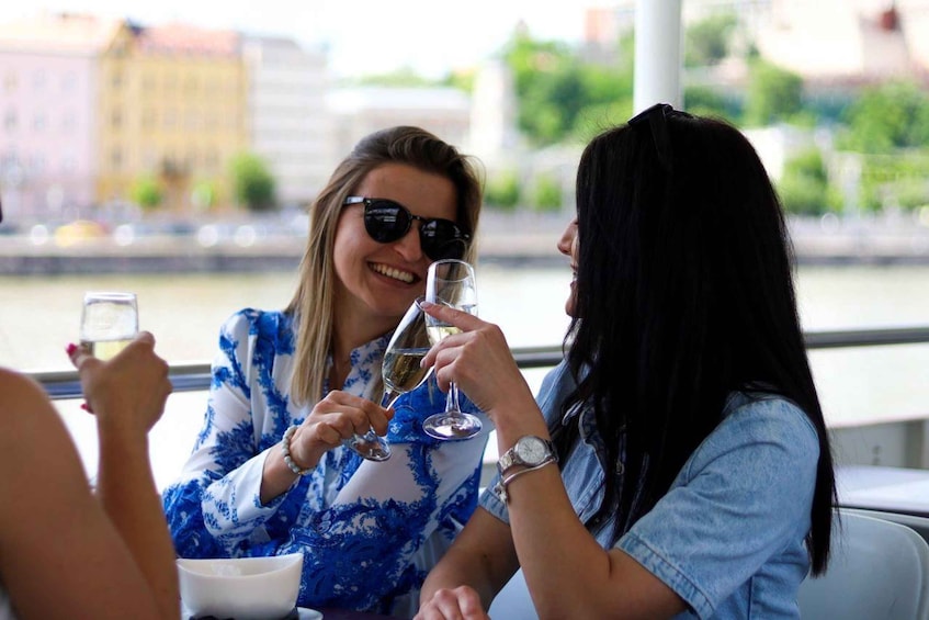 Two people toasting with champagne glasses at a table by a river. 1
