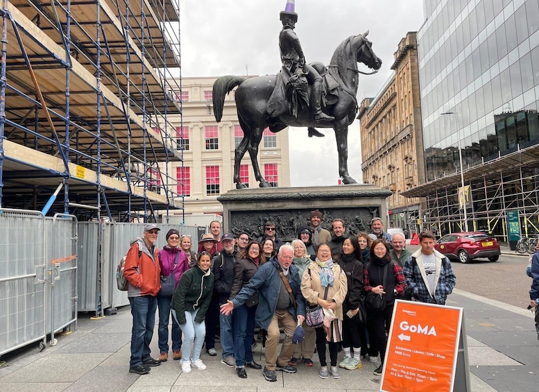 A group of people posing in front of a statue of a man on a horse, with a modern building and scaffolding in the background. 3