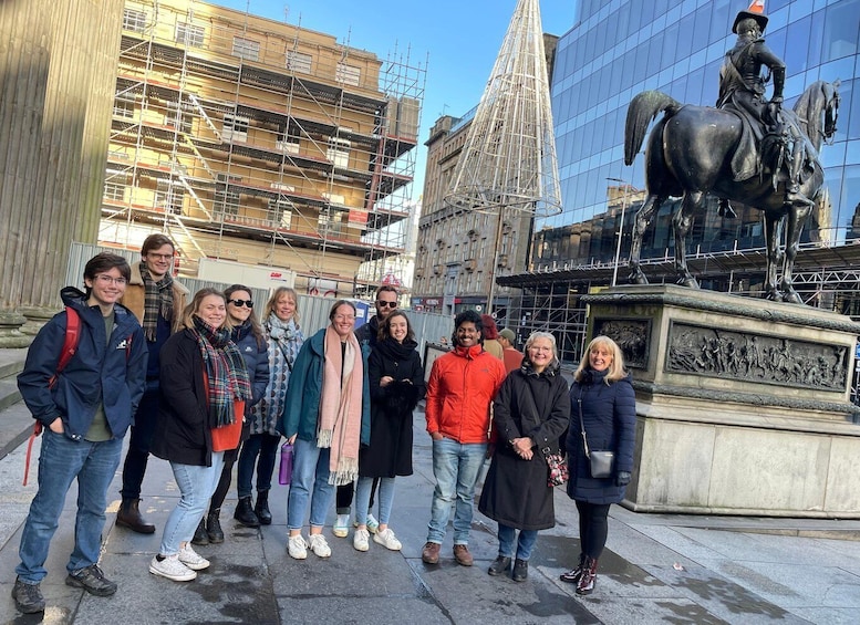 A group of people standing in front of a statue of a man on a horse, with a building under construction in the background. 1