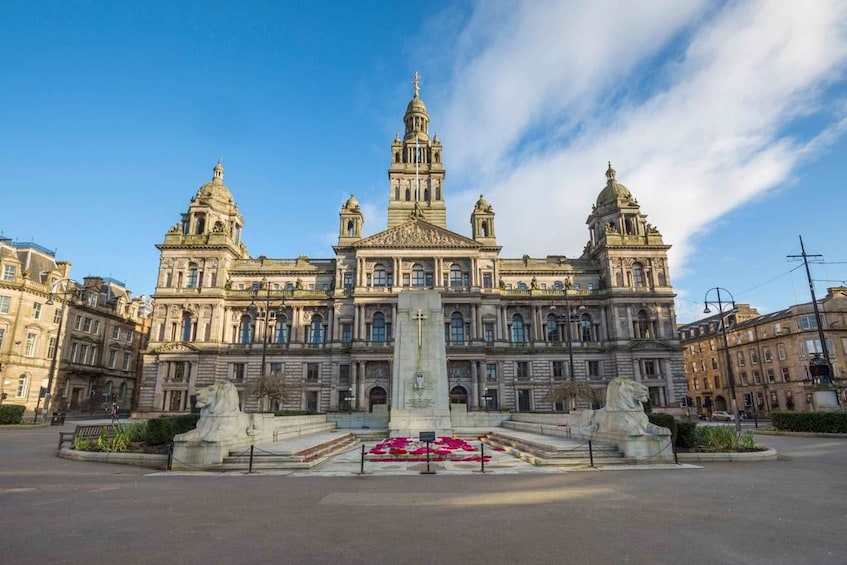 A grand neoclassical building with a central dome and two smaller domes, a large statue in front, and a statue of a lion on either side. 2