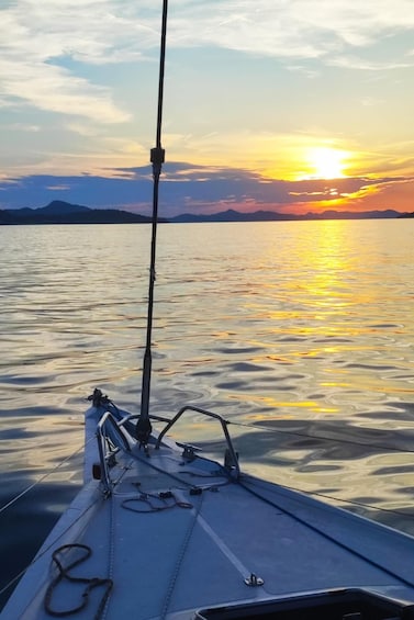 Bådens bue med mast og rig, rolig vandflade og en solnedgang over et fjerntliggende landskab. 2
