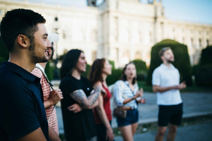 A group of people standing in a line on a street with a large building in the background. 4