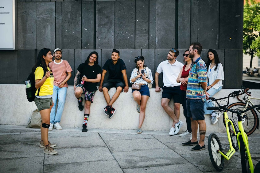 A group of people sitting and standing against a wall, with a bicycle leaning against the wall. 5