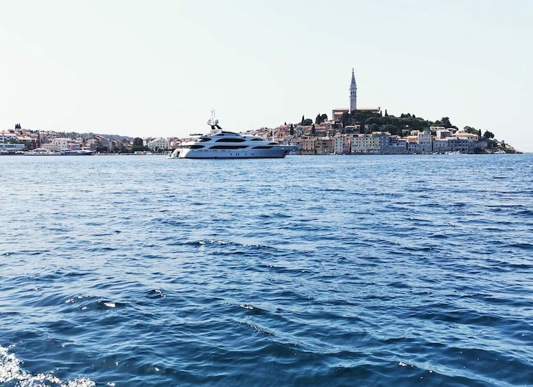 A large yacht on calm waters with a historic town and a prominent tower in the background. 4