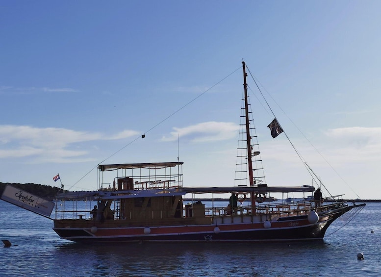 A traditional sailing boat with a tall mast and a cabin structure, docked at a calm body of water. 5