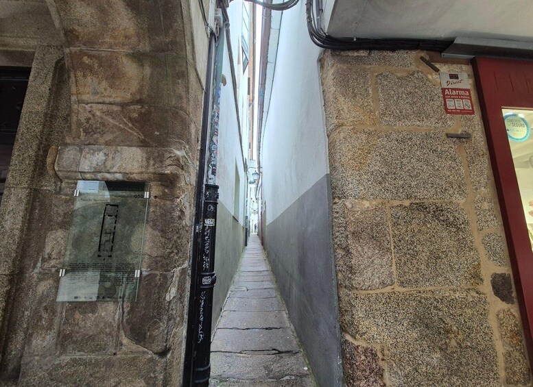 A narrow alleyway with stone walls, a glass door, and a red door with a sign. 2