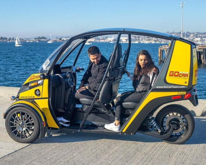 A yellow and black GoCar parked by the waterfront with a cityscape in the background. 1