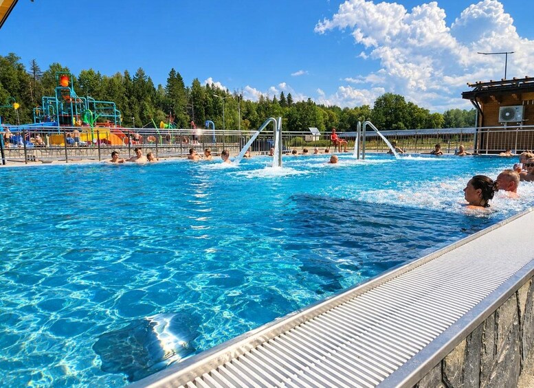 Une piscine avec des personnes dans l’eau, un toboggan aquatique et, au fond, une zone boisée. 5