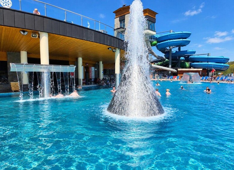 A swimming pool with a central water fountain, a water slide, and people swimming. 5