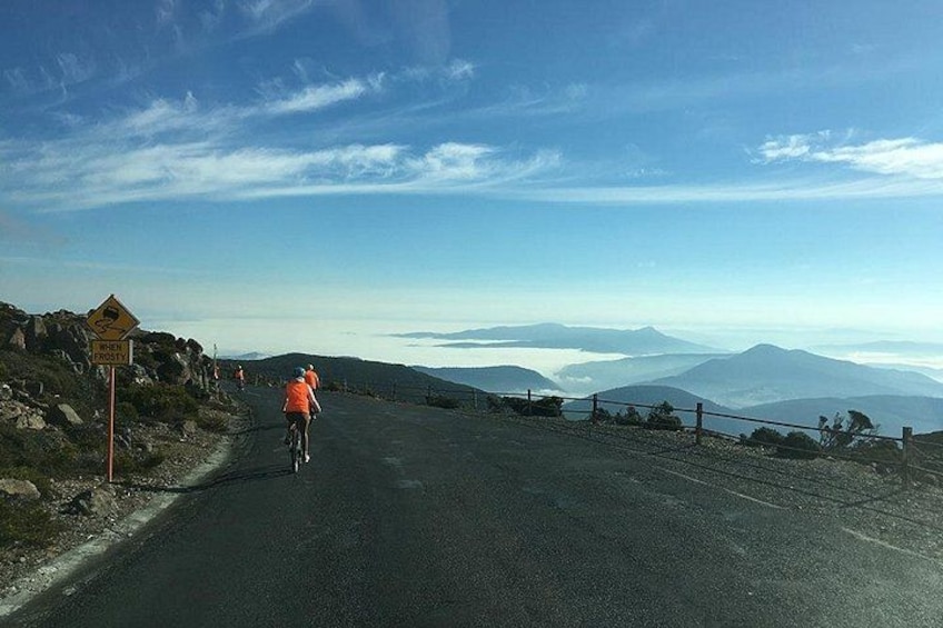 A cyclist on a mountain road with a view of distant mountains under a clear sky. 2
