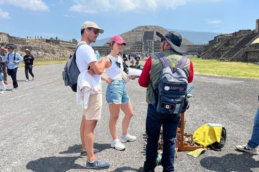 Tourists at an archaeological site with ancient ruins and a large stone structure in the background. 1