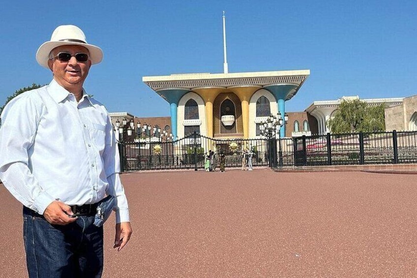 A man in a white hat and shirt standing in front of a building with a tall tower. 1