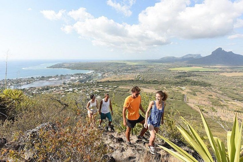 Un grupo de personas caminando por un sendero montañoso, con vista a un paisaje costero y una montaña al fondo. 5