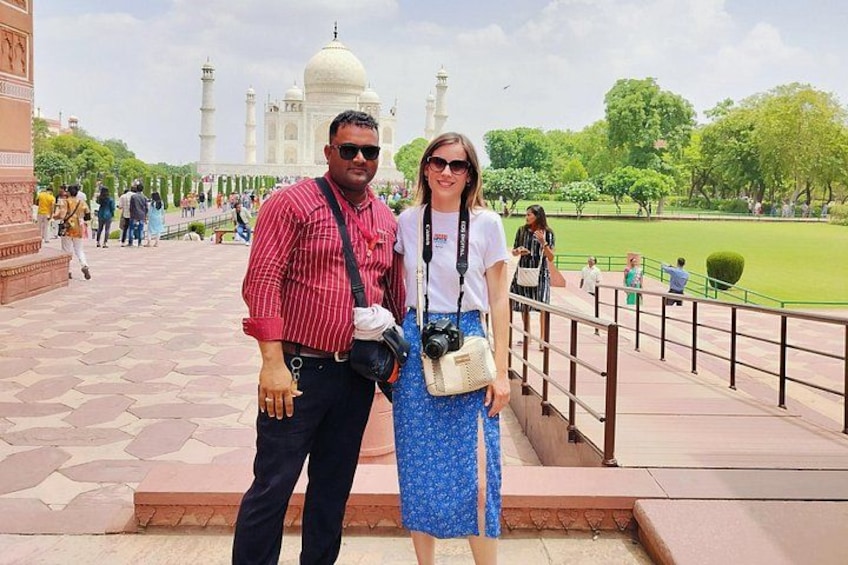 A couple standing in front of a large white dome structure with minarets, surrounded by a park with trees and a paved walkway. 4