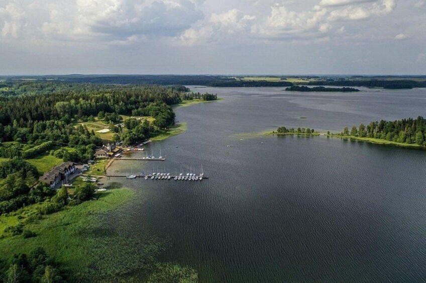 Un lago rodeado de zonas boscosas, con un pequeño muelle y edificios a la izquierda. 2