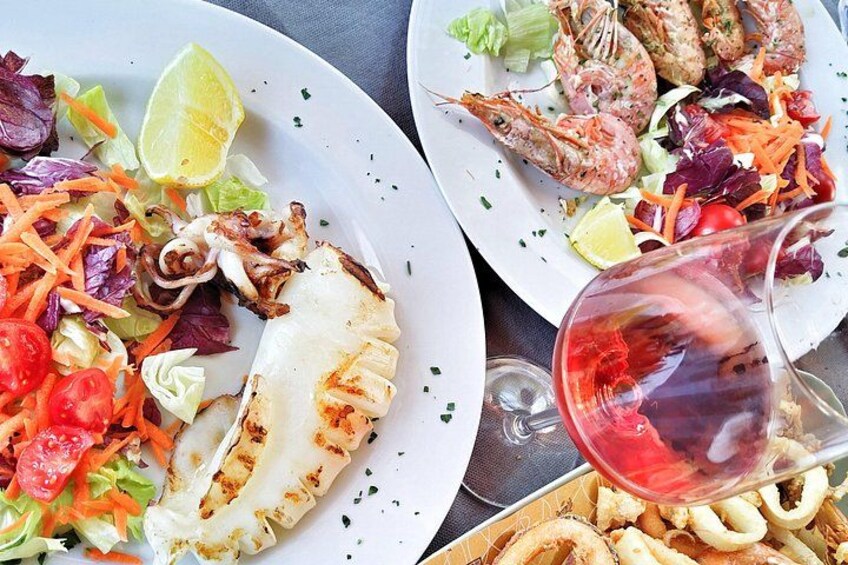 Un plato de pescado a la parrilla, camarones y ensalada, acompañado de una copa de vino tinto. 2