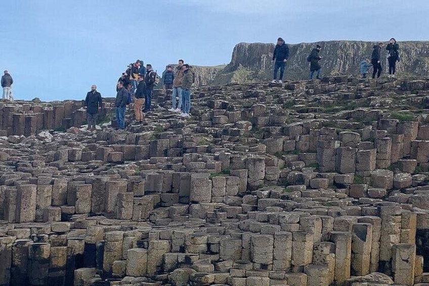 A group of people standing on a rocky outcrop with a large cliff in the background. 2