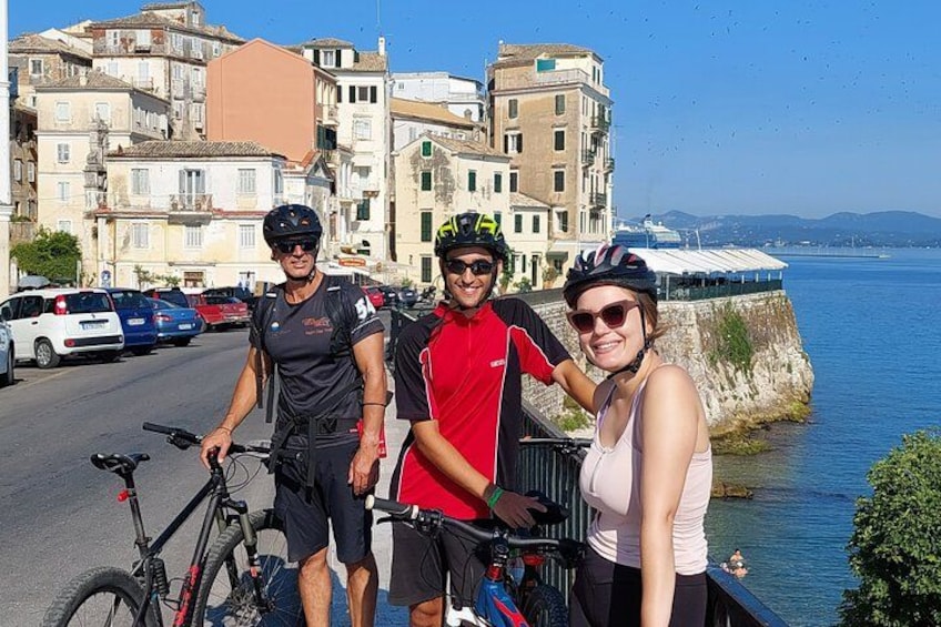 Tres personas con bicicletas, un frente marítimo y edificios al fondo. 4