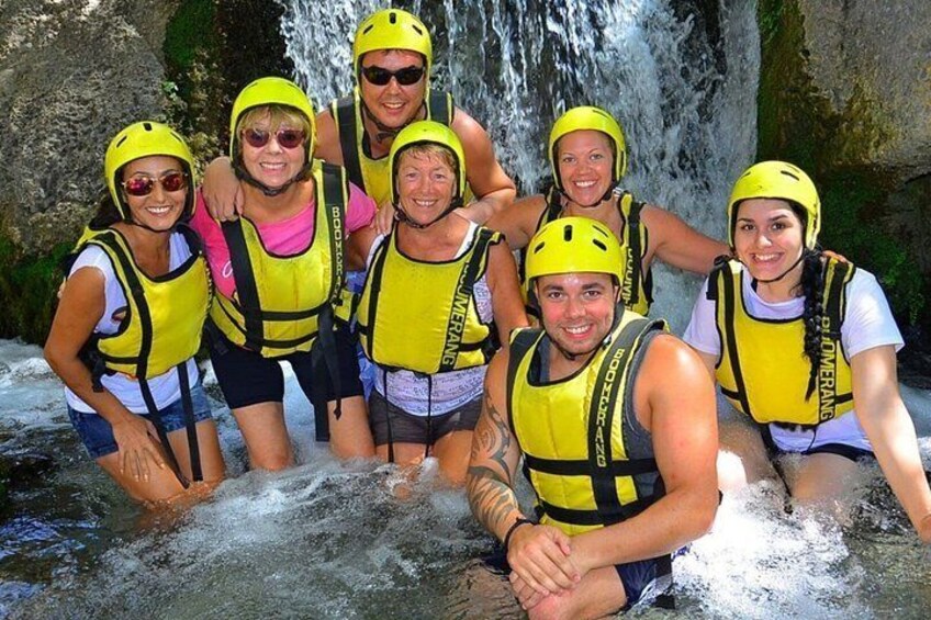A group of people wearing yellow life jackets and helmets, standing in front of a waterfall. 3