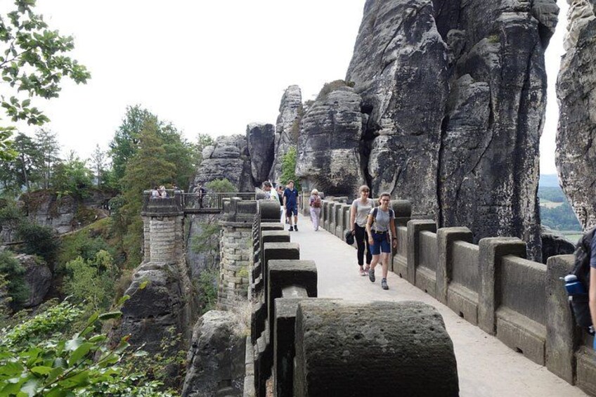 A stone bridge with people walking on it, surrounded by rocky cliffs and greenery. 3