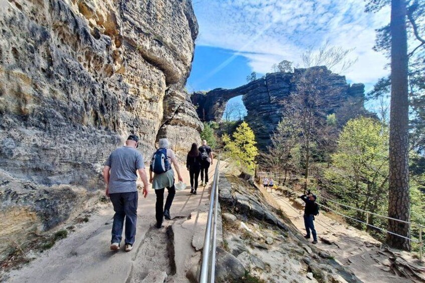 Hikers on a rocky trail with a natural rock formation in the background. 2