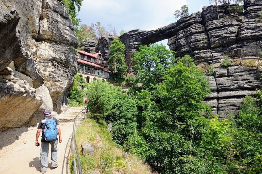 Un sendero para excursionismo con una gran formación rocosa y un edificio al fondo. 5