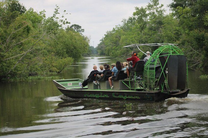 A green boat with passengers, surrounded by dense greenery and calm water. 2