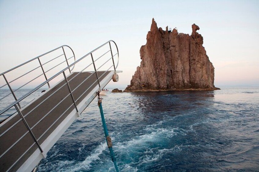 A rocky outcrop in the ocean with a ship's railing in the foreground. 2