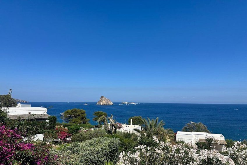 A coastal landscape with white buildings, a rocky outcrop, and a clear blue sky. 2