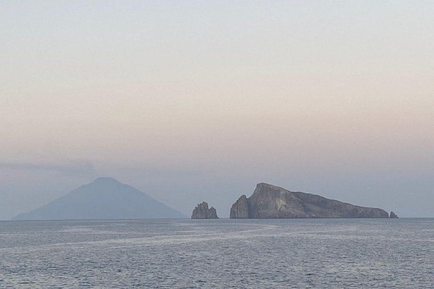 A calm sea with a distant mountain and a rocky outcrop. 5